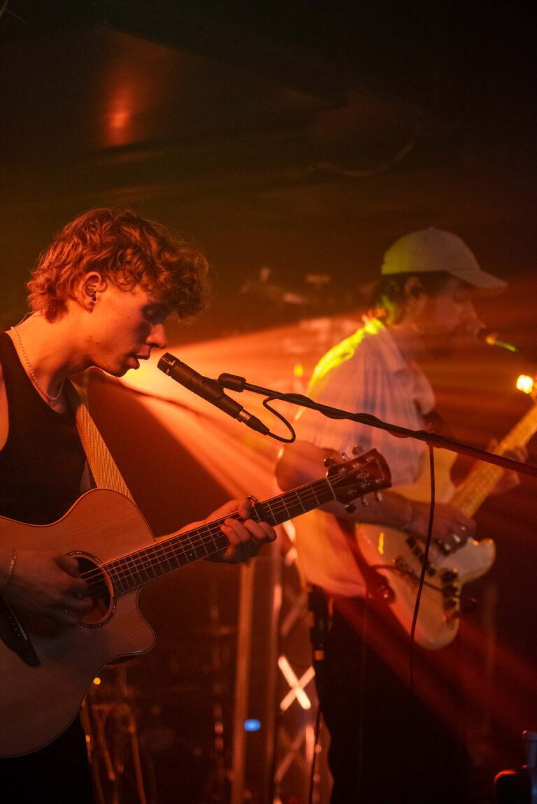 Zwei Musiker spielen auf einer Bühne. Die Szene ist in orangenes Licht getaucht.