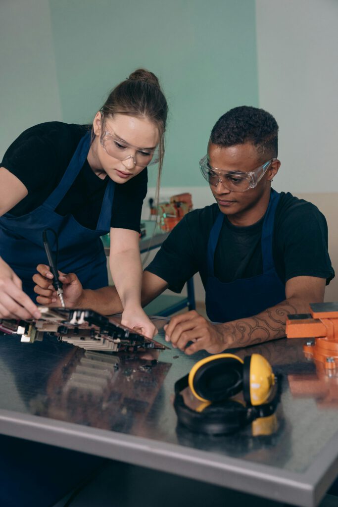 Eine Auszubildende und ein Auszubildender arbeiten an einem elektronischen Apparat in ihrer Ausbildung.